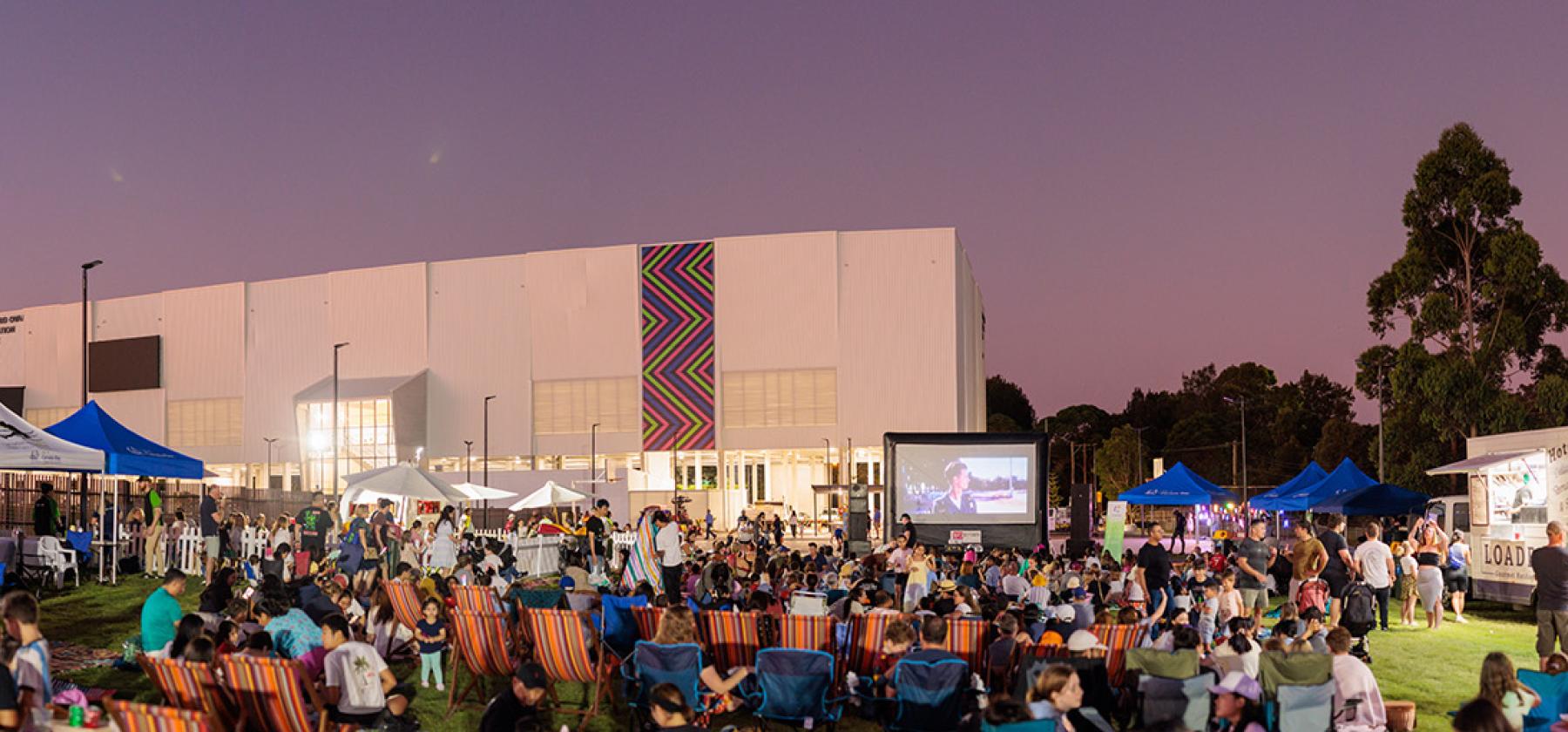 The sun sets over a large crowd infront of the Concord Oval Recreation Centre