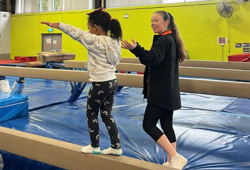 Child and coach balancing on a gymnastics beam